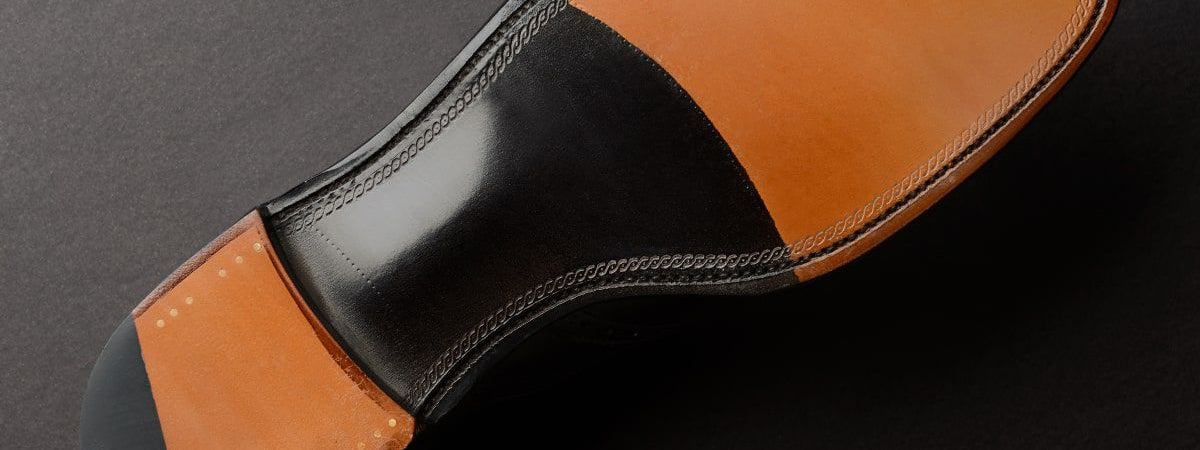 Close-up of a shoe's sole showcasing Goodyear welt construction. Tan leather meets black leather with delicate stitching, conveying quality and craftsmanship.